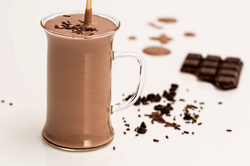 large glass mug of chocolate smoothie with chocolate sprinkles and half of a bar of chocolate